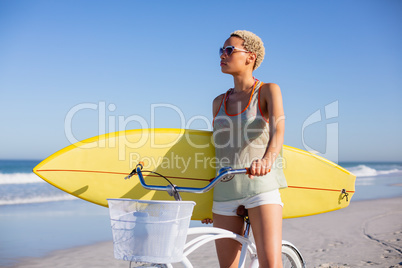 Woman with surfboard sitting on bicycle at beach in the sunshine