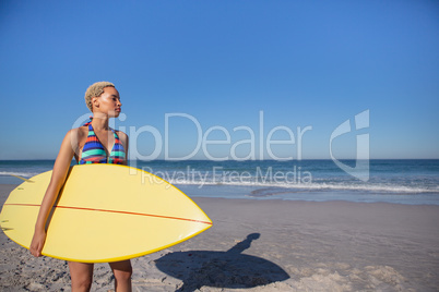 Beautiful woman in bikini standing with surfboard on beach in the sunshine