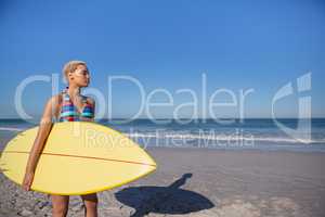 Beautiful woman in bikini standing with surfboard on beach in the sunshine