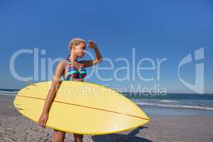 Beautiful woman in bikini with surfboard shielding eyes on beach in the sunshine