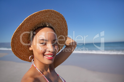 Happy woman in bikini and hat looking at camera on beach in the sunshine