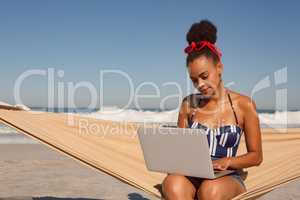 Beautiful woman using laptop on hammock at beach in the sunshine