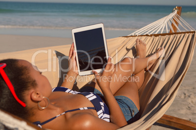 Woman using digital tablet while relaxing on hammock on beach