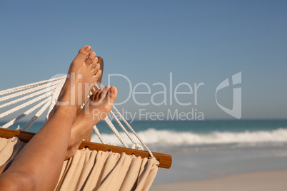 Low section of woman relaxing on hammock at beach
