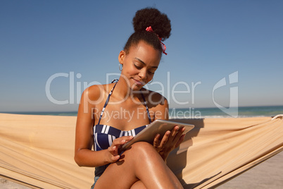 Woman using digital tablet while sitting on hammock at beach in the sunshine