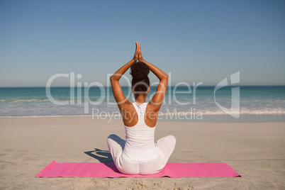 Woman doing yoga on exercise mat at beach in the sunshine