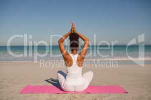 Woman doing yoga on exercise mat at beach in the sunshine