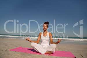 Beautiful woman doing yoga on exercise mat at beach in the sunshine
