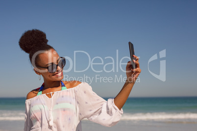 Beautiful woman taking selfie with mobile phone at beach in the sunshine