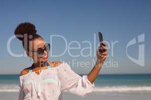 Beautiful woman taking selfie with mobile phone at beach in the sunshine