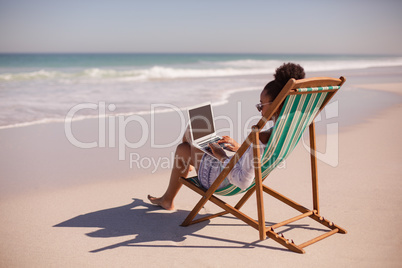 Woman sitting on beach chair and using laptop at beach in the sunshine