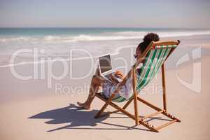 Woman sitting on beach chair and using laptop at beach in the sunshine