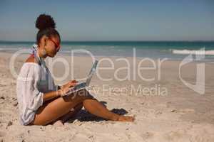 Woman sitting on sand and using laptop at beach in the sunshine