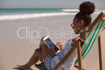 Woman sitting on beach chair and using digital tablet at beach in the sunshine