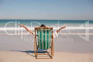Woman with arms stretched out sitting on beach chair at beach in the sunshine