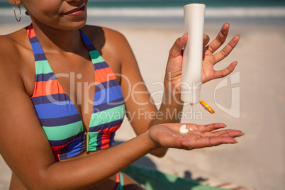 Woman in bikini applying sunscreen lotion at beach in the sunshine