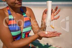 Woman in bikini applying sunscreen lotion at beach in the sunshine