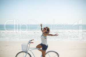 Woman riding bicycle with arms outstretched on the beach