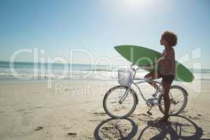 Woman holding a surfboard with bicycle at beach
