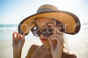Beautiful woman in hat looking over sunglasses on the beach