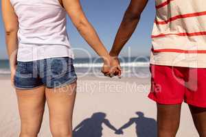 Couple holding hands and standing on beach in the sunshine