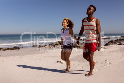 Couple holding hands and walking on beach in the sunshine