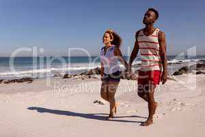 Couple holding hands and walking on beach in the sunshine