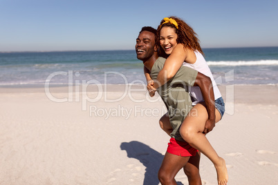 Man giving piggyback to woman on beach in the sunshine