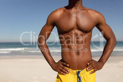 Shirtless man with hands on hip standing on beach in the sunshine