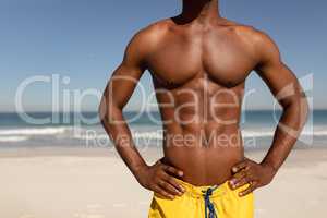 Shirtless man with hands on hip standing on beach in the sunshine