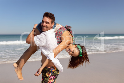 Man carrying woman on shoulders on beach in the sunshine