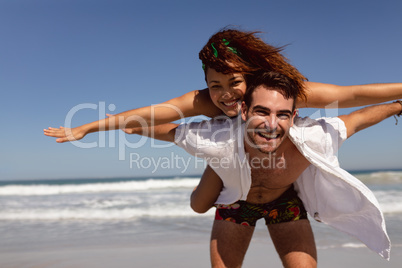 Man giving piggyback to woman on beach in the sunshine