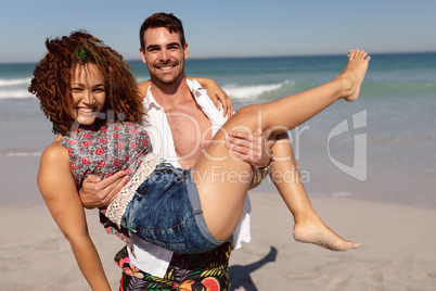 Young man holding woman in his arms on beach in the sunshine