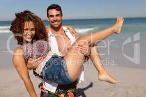 Young man holding woman in his arms on beach in the sunshine