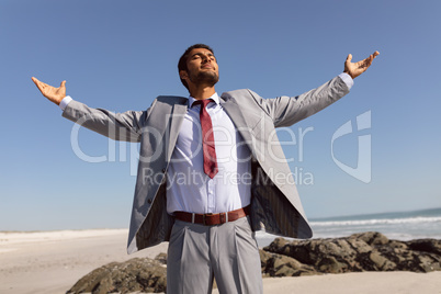 Businessman standing with arms outstretched and eyes closed on the beach