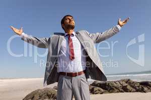 Businessman standing with arms outstretched and eyes closed on the beach