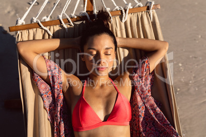 Woman sleeping with hands behind head in a hammock on the beach