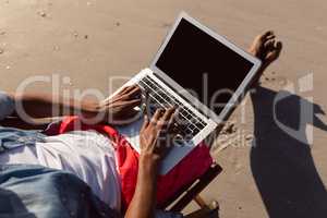 Man using laptop while relaxing in a beach chair on the beach