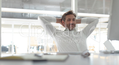 Business male executive with hands behind hand sitting at desk in a modern office