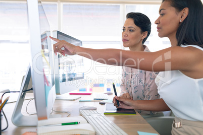 Female graphic designers discussing on computer at desk in a modern office