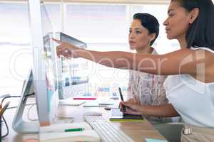 Female graphic designers discussing on computer at desk in a modern office