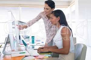 Female graphic designers discussing on computer at desk in a modern office