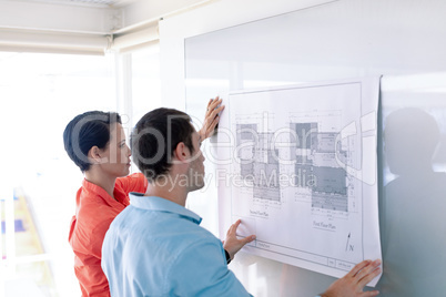 Architects discussing over blueprint on glass board in a modern office