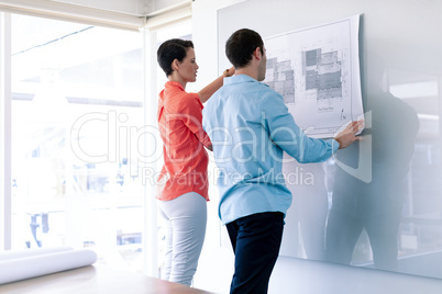 Architects discussing over blueprint on glass board in a modern office