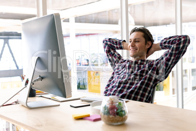 Male graphic designer with hands behind head sitting on chair in a modern office