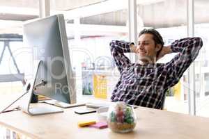 Male graphic designer with hands behind head sitting on chair in a modern office