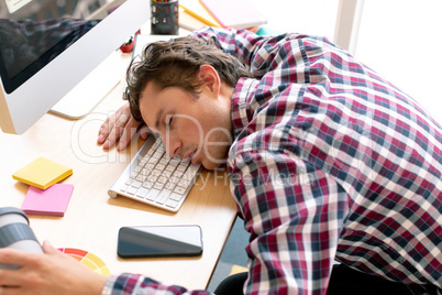 Male graphic designer sleeping on desk in a modern office