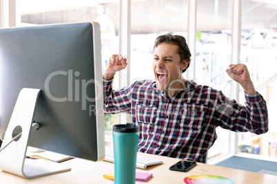 Male graphic designer celebrating success at desk in a modern office