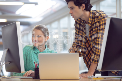 Male and female graphic designer discussing over computer