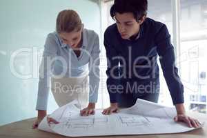 Male and female architects discussing over blueprint in office